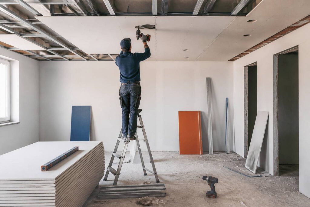 Artisan posant un plafond suspendu en plaques de plâtre sur ossature métallique dans une pièce en rénovation