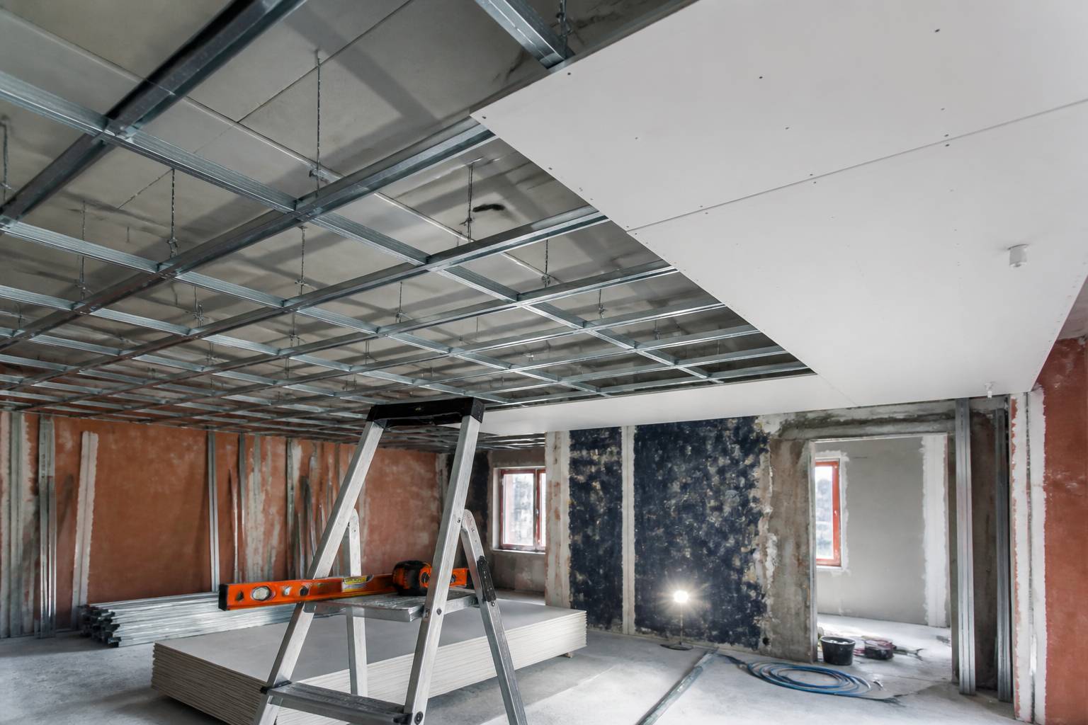 Ossature métallique de plafond suspendu avec suspentes, rails et plaques de plâtre partiellement vissées